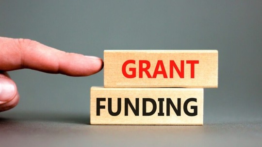 2 wooden blocks on top of one another with the words 'grant' and 'funding' on them. A finger points at them.