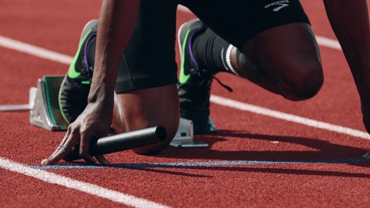 A cut off image of a runner on the starting blocks. Only his hands and legs and the running track are visible.