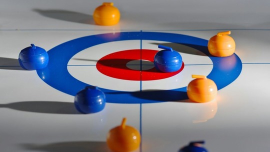 An indoor curling target with blue and yellow curling stones scattered across it