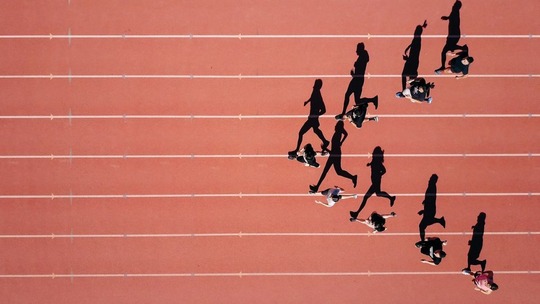 A group of 8 runners seen from above on a running track. The runners form a 'V'.