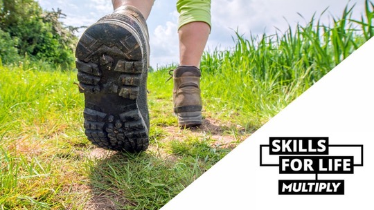 A pair of walking boots seen in extreme close up, walking through grass. Skills for Life Multiply logo in bottom right corner.