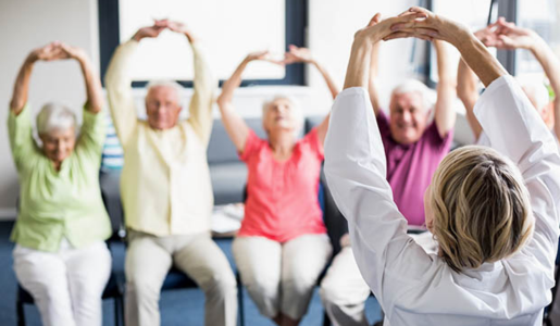 6 older people, men and women, doing seated stretches. They all have their arms stretched above their heads.