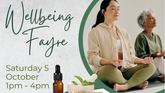Image of 2 women doing sitting meditation. Text to left of image reads: Wellbeing Fayre Saturday 5 October 2024 1pm - 4pm.