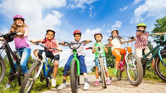 A group of 6 boys and girls of different ages on bikes and wearing colourful clothing and helmets