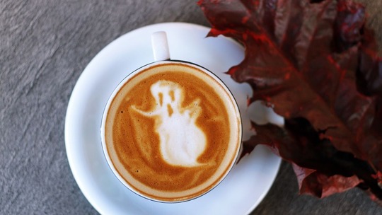 A foamy cup of coffee seen from above, on a wooden table with autumn leaves around the right hand edge