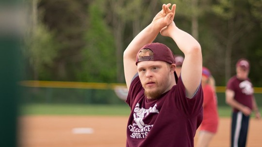 A young man with Down Syndrome on a running track, stretching his arms above his head.