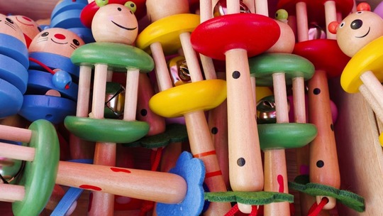 Children's wooden rattles and rain sticks, all painted in primary colours.
