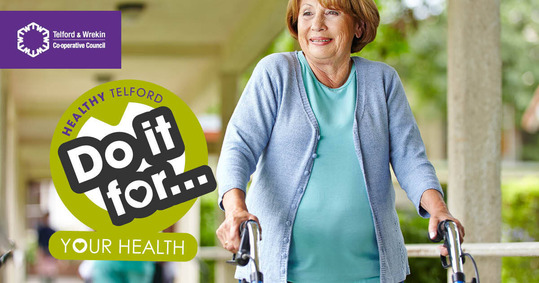 An older woman walking with a zimmer frame, over which the black Do It For logo and text appear.