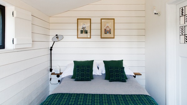 Double bed with green cushions in small white room