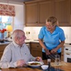 A carer serving a mealy to an elderly man
