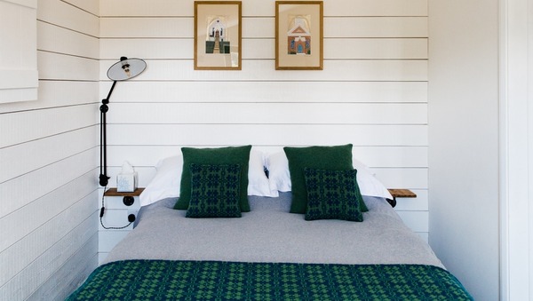 Double bed with green cushions in small white room