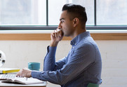 Adult at a table with a coffee mug and a notebook, looking at a laptop screen.