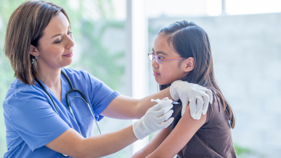 A girl aged around 9 years old being vaccinated by a medical professional in scrubs