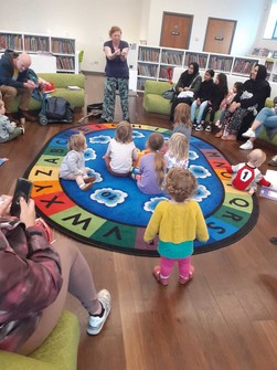 Children and adults sitting and standing inside the children's library in Walthamstow library participating in world singing day