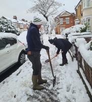 Two people clear snow from a pavement