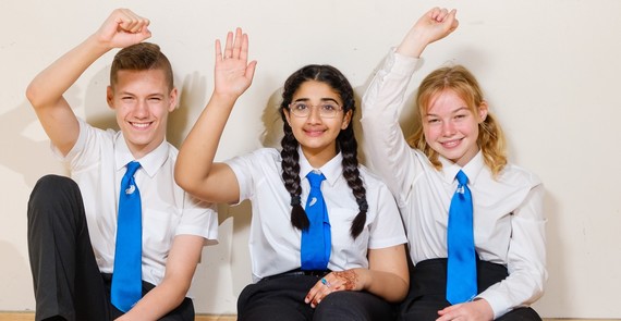 Three school students sit with their hands up