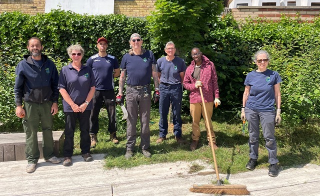 A group of volunteers post with a big broom in front of a hedge