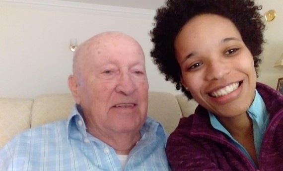 An elderly man sits next to a younger person, smiling
