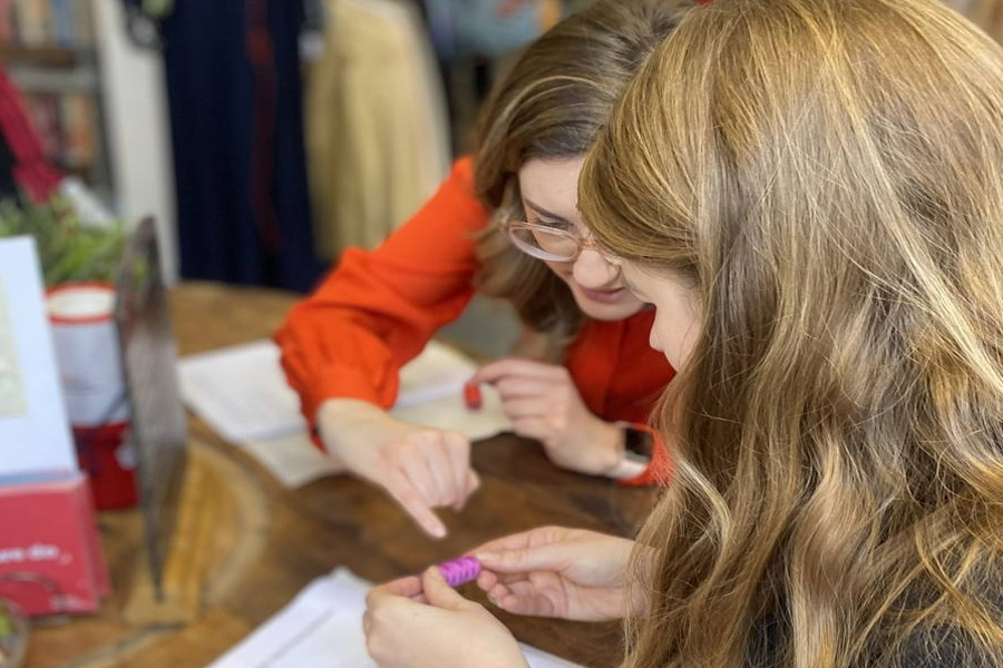 A person points at a spool of pink cotton in another person's hand