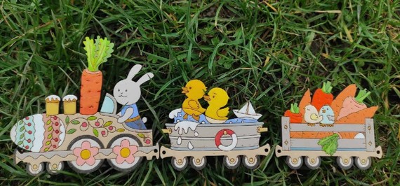 A bunny rabbit drives a felt train with a carrot as a funnel and chicks for passengers