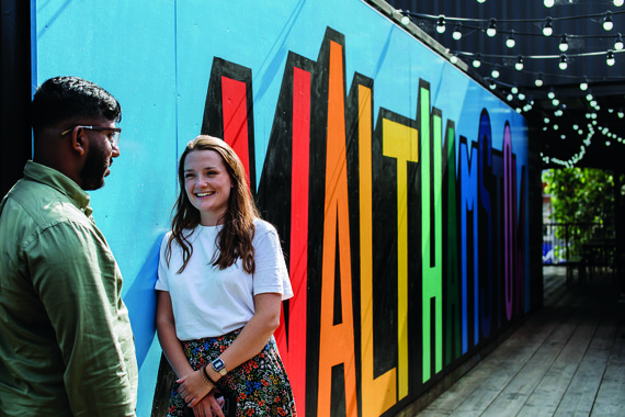 A young woman and man chat in front of street art spelling out Walthamstow