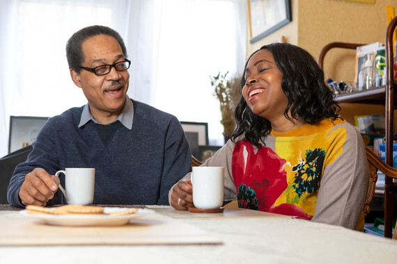 Foster carers Julien and Pauline sit at a table holding mugs in their hands