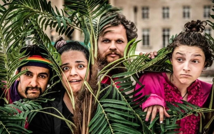 Four people from the East London Shakespeare Festival peer through the leaves of plants