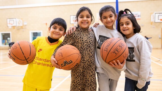 Young children pose with a basketball on a court 