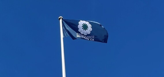 Blue flag with a white circle and the message Remember Srebrenica flying on a flag pole against a brilliant blue sky
