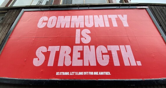 A billboard in London saying Community is Strength in large pink letters on a red background