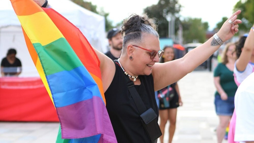 A smiling person at the 2022 Waltham Forest Pride event holds up a rainbow flag