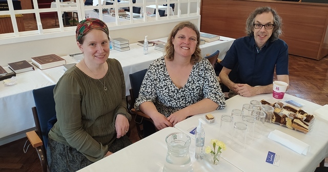 Three people sit at a table looking a the camera in a community living room. Cllr Williams sits in the middle.
