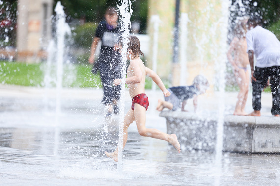 A child in swimming shorts runs through a jet of water in the Fellowship Square fountain