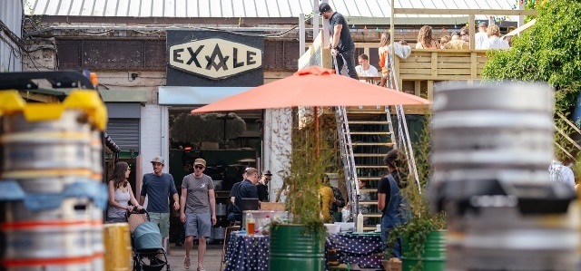 Exterior shot of Exhale Brewery with customers sitting at a table under an umbrella, and beer kegs piled up