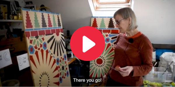 A woman stand in front of large patterns on two boards. Subtitles say 'There you go'