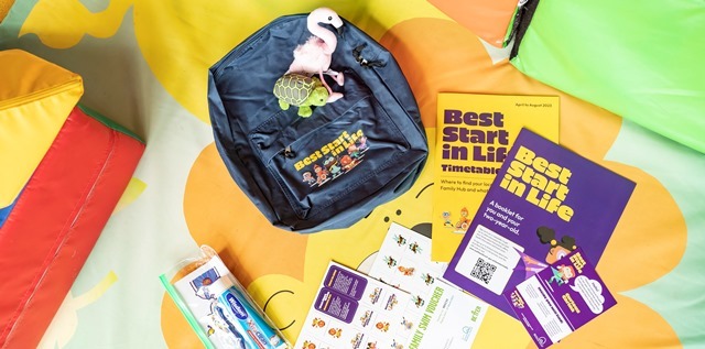 A back pack lies on a flat surface surrounded by stickers, small toys and other stationery