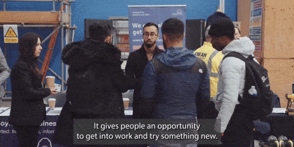 Young people talking to stallholders at desks in a large room at a jobs fest with lots of other people