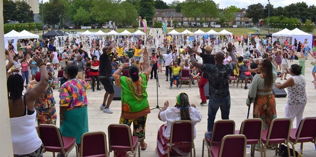 A group of people perform for the crowd in front of Waltham Forest Town Hall, looking over the fountain area and grass