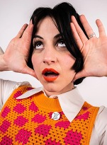 Close up on a woman wearing a bright orange checked tank top, looking up with her hands either side of her face