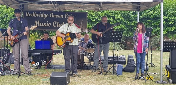 The band Replay band featuring a vocalist, guitarists, keyboard and drums play in a tent outside on grass