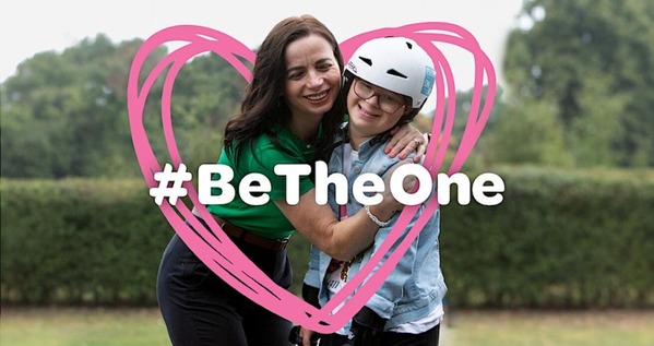 A woman hugs a child. They are wearing a cycle helmet. Both have a pink heart drawn around them. #BeTheOne fostering campaign