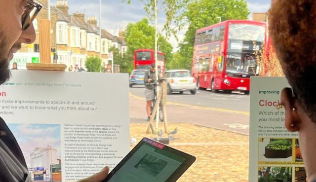 Two people look at engagement boards about Markhouse Corner. Traffic and a cyclist are shown in the background