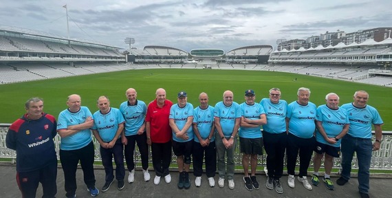 The walking cricket team line-up with the Lords pitch and stand behind them