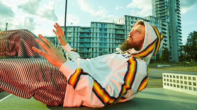 A man in a white hoodie lies on the ground with high rise buildings behind him