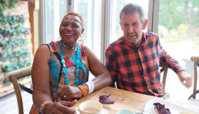 A man and woman sit drinking a hot drink at a table, smiling.