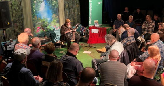 A seated guitarist performs in front of an audience at Walthamstow Folk Club