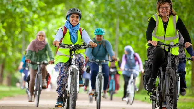 A group of women smile as they cycle along a tree-lined path