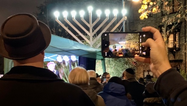 A member of the crowd looks at the fully lit menorah through their mobile phone screen