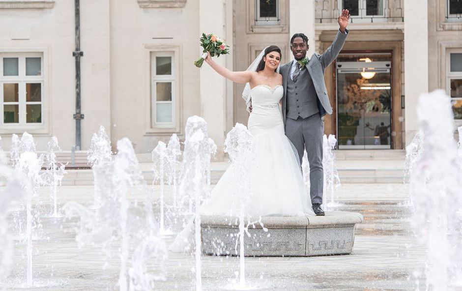 A couple wave from the middle of the fountain in Fellowship Square