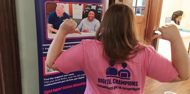 A person points with both thumbs to the Digital Champions logo on the back of their shirt